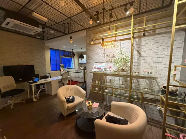 Lounge with a neon parlor sign, gold shelves, and cream chairs, with reception beyond.