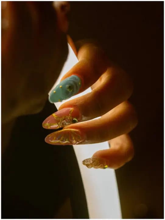 A hand with turquoise, pink, and gold nail art held around a bright light.