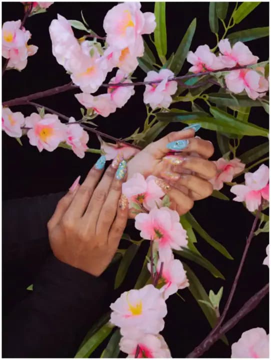 Hands with glitter and rhinestone nail art held among pink blossoms, photographed for the parlor.