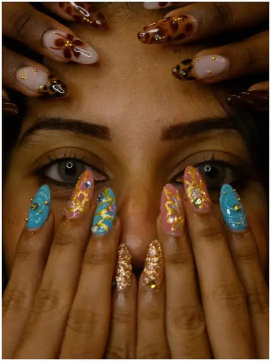 A person’s face framed by two sets of decorated nails, including floral, leopard print, and gold work.