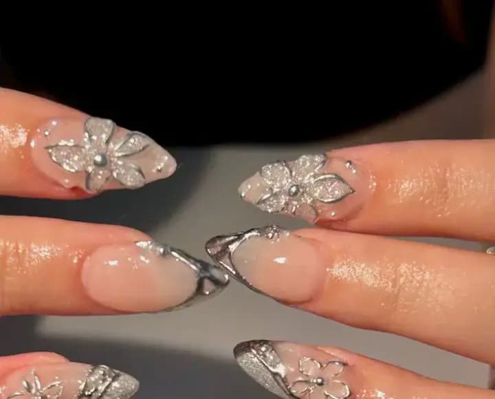 Close-up of nude-pink almond nails with raised silver floral detail and chrome tips from the parlor.