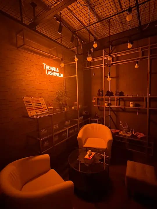 Cream chairs and a glass table in the lounge under warm light, with the neon sign and polish shelves.
