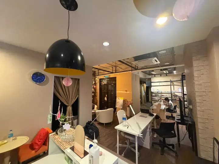 Open salon floor from reception toward the manicure stations, with a technician at work.