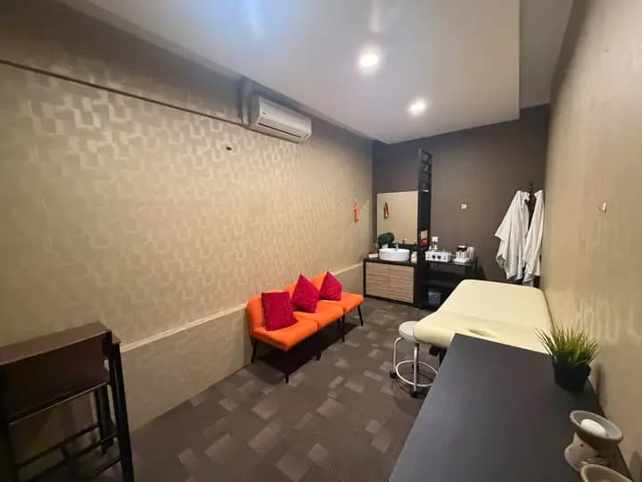 Private room with orange chairs, red pillows, a treatment bed, a sink, and white robes.