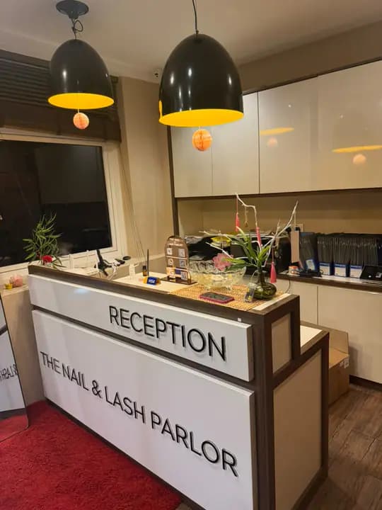 Reception desk with the parlor name on the front, a black and gold pendant light, and a red rug.