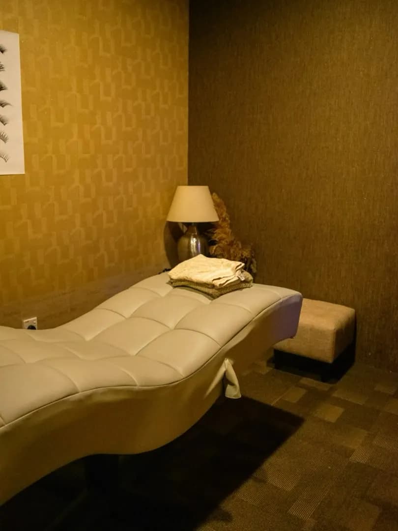 Corner of the lash bed with a folded textile, a lamp, and gold patterned wallpaper.