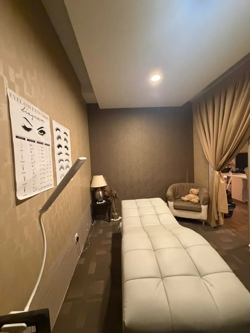 Lash treatment room with a tufted bed, a lamp, and an eyelash extension diagram on the wall.