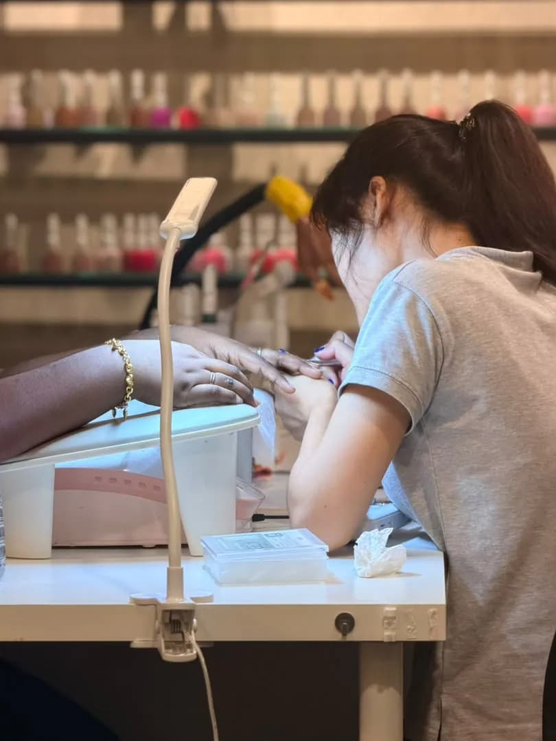 A manicure in progress at a white station, with a task lamp and a wall of polish.